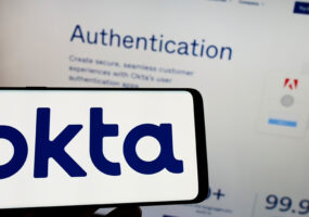 Okta, Person holding cellphone with logo of US identity management company Okta Inc. on screen in front of business webpage.