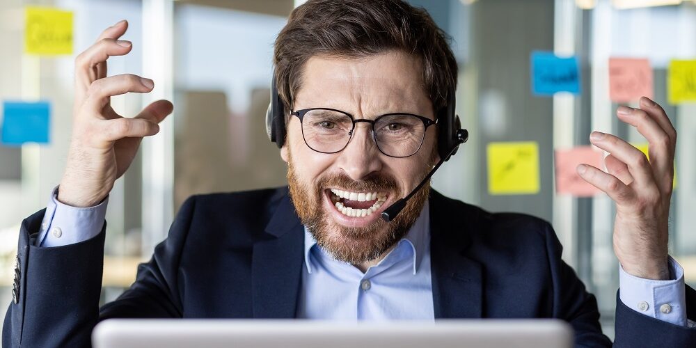 An overwhelmed businessman in a headset shows frustration while working at his desk filled with sticky notes in a modern office.