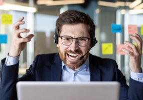 An overwhelmed businessman in a headset shows frustration while working at his desk filled with sticky notes in a modern office.