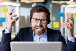 An overwhelmed businessman in a headset shows frustration while working at his desk filled with sticky notes in a modern office.