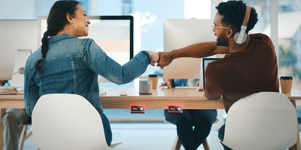 Rearview shot of two young designers giving each other a fist bump in an office, on display is Crestron desk scheduling device