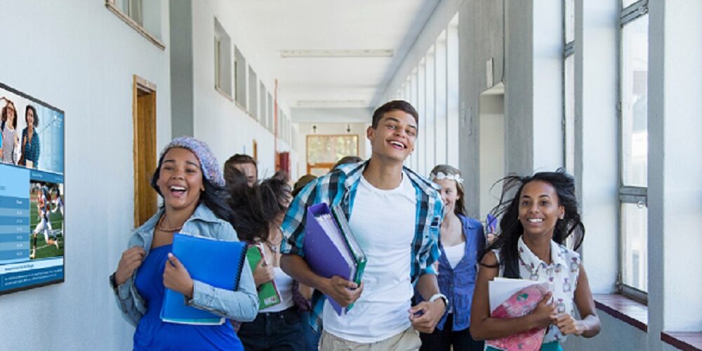 Students running down a campus hall and following signs on a Samsung digital display.