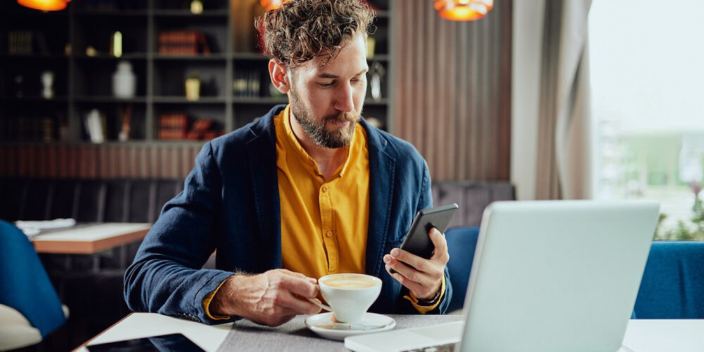 man looking at phone while working and sipping on cofee, GoTo Resolve RMM Tool