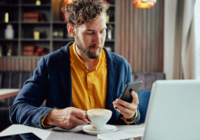 man looking at phone while working and sipping on cofee, GoTo Resolve RMM Tool